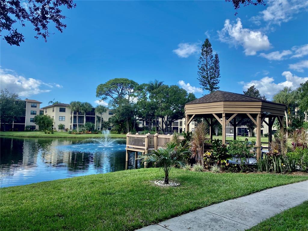 A gazebo sits beside a pond with a fountain near a multi-story apartment building — 315 30TH AVENUE W UNIT B305, BRADENTON, FL