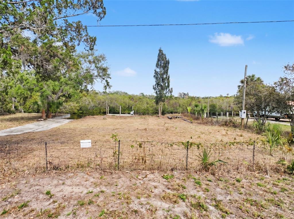 A vacant, fenced-in waterfront lot features a concrete boat ramp and mature trees — LOT 8 RICE ROAD, HUDSON, FL