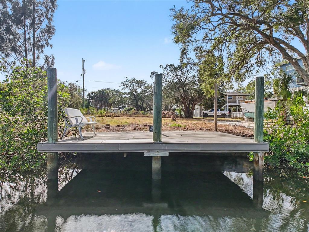 A wooden dock with a white chair extends over calm water toward a grassy lot — LOT 8 RICE ROAD, HUDSON, FL
