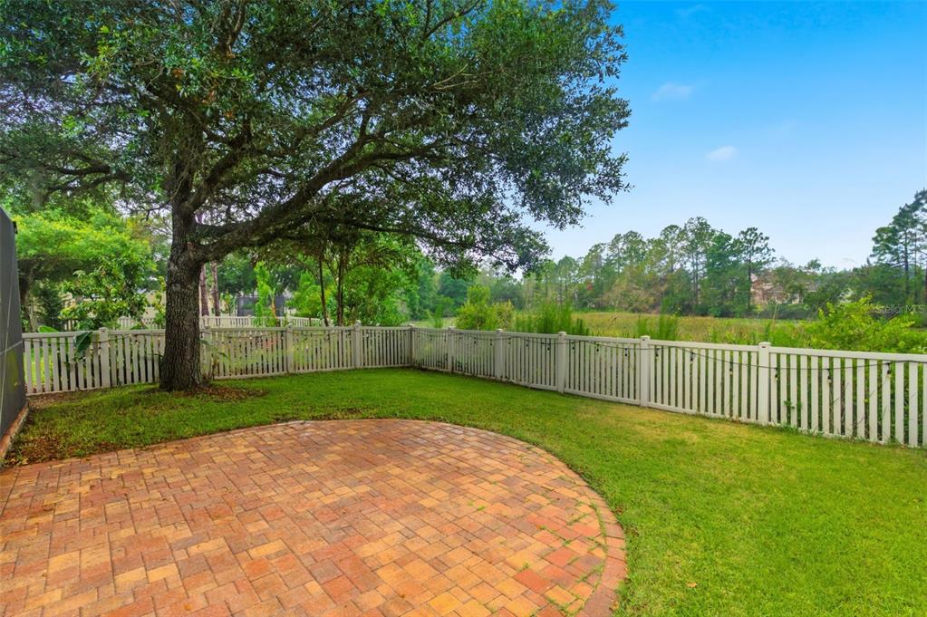 A backyard features a circular brick paver patio, a large tree, and a white fence — 21347 MORNING MIST WAY, LAND O LAKES, FL