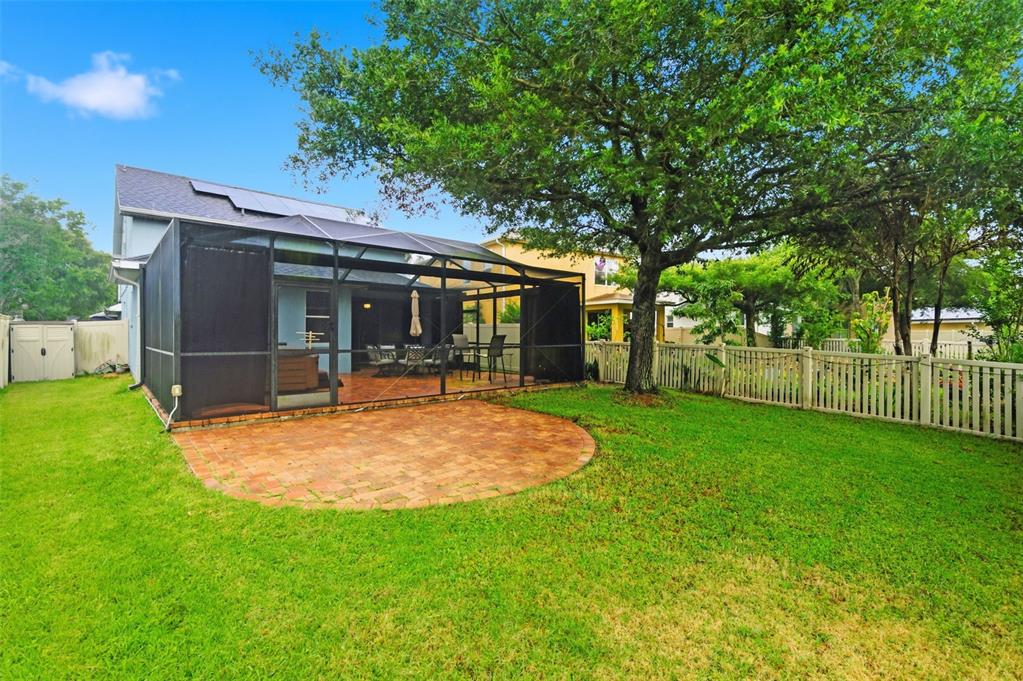 A backyard features a brick patio, a screened-in porch, a large tree, and white fencing — 21347 MORNING MIST WAY, LAND O LAKES, FL