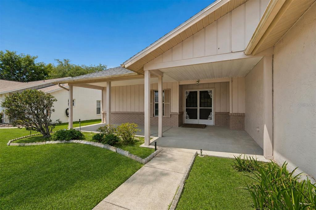 A covered concrete patio leads to a double-door entrance of a single-story suburban home — 4643 SANDPOINTE DRIVE, NEW PORT RICHEY, FL