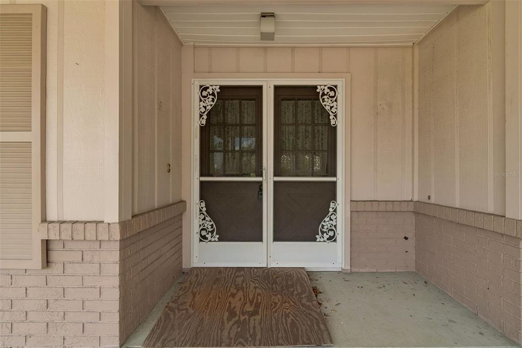 A covered entryway features a double screen door with decorative corner scrollwork and brick siding — 4643 SANDPOINTE DRIVE, NEW PORT RICHEY, FL