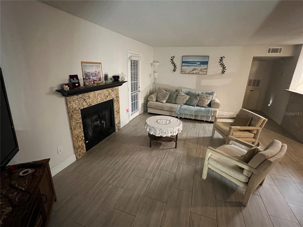 A living room features a fireplace with a granite surround, tile flooring, and neutral furniture — 5587 DEVONBRIAR WAY UNIT J105, ORLANDO, FL