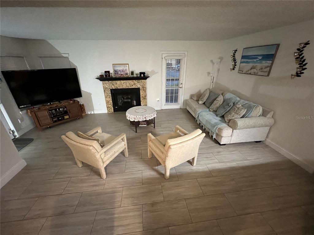 A living room features a fireplace, a sofa, two armchairs, and light wood-look tile flooring — 5587 DEVONBRIAR WAY UNIT J105, ORLANDO, FL