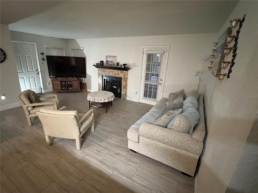 A living room features tile flooring, a fireplace with a stone surround, and a sofa — 5587 DEVONBRIAR WAY UNIT J105, ORLANDO, FL