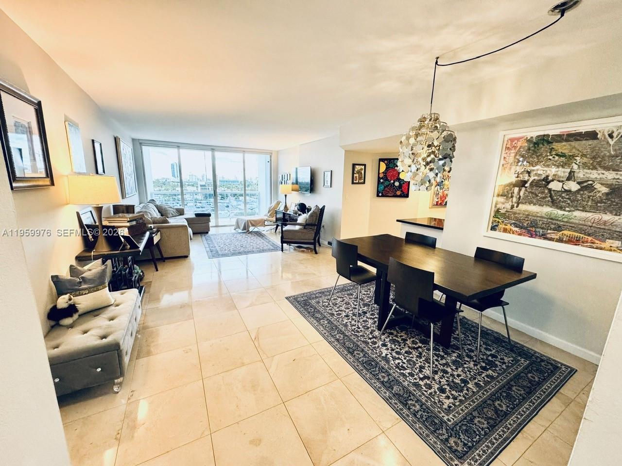 A modern open-plan living and dining area features tile floors, a chandelier, and balcony views — 1900 Sunset Harbour Dr # 1009, Miami Beach FL 33139, MIAMI BEACH, FL