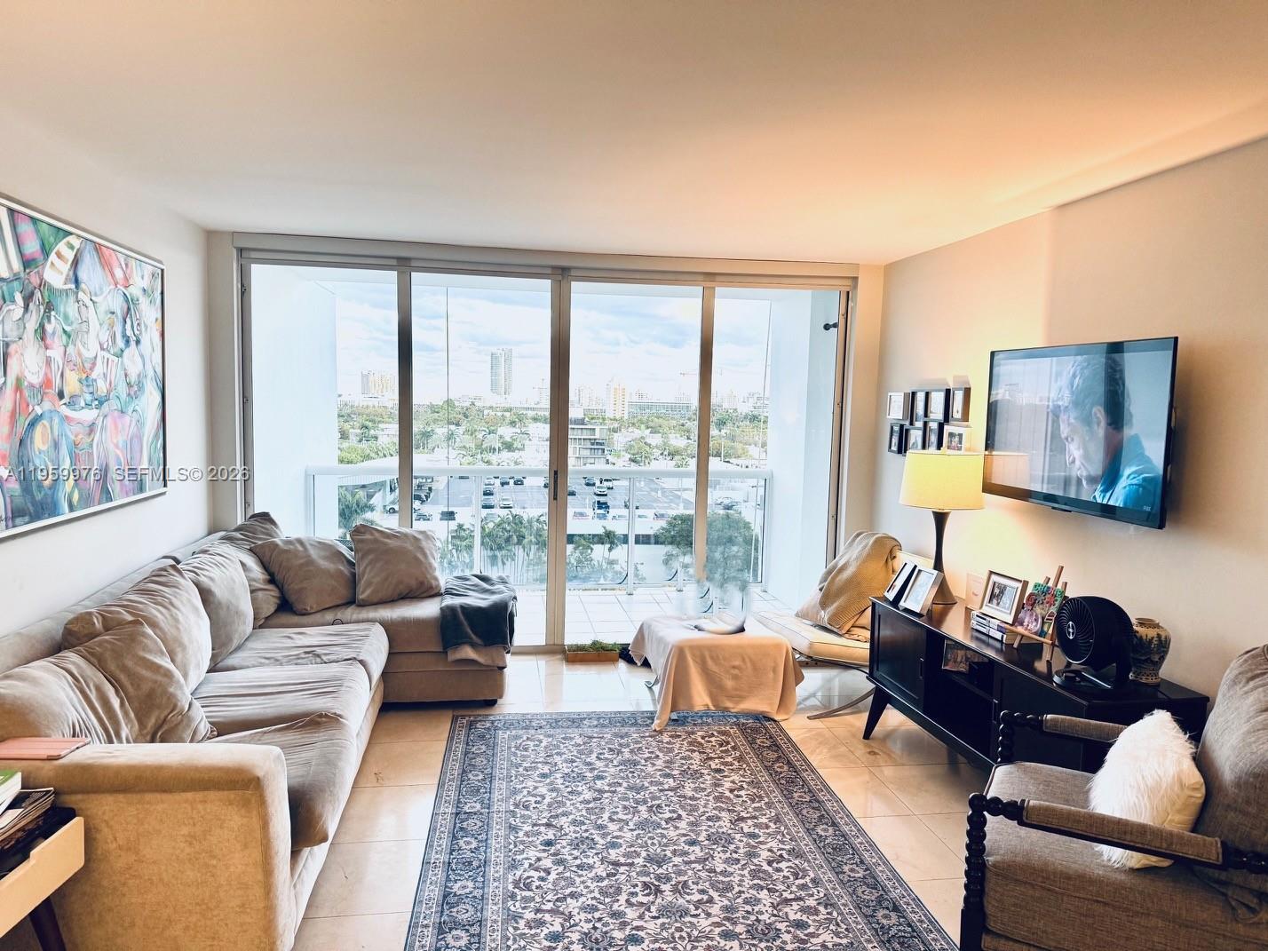A living room features a sectional sofa, a patterned rug, and a balcony with city views — 1900 Sunset Harbour Dr # 1009, Miami Beach FL 33139, MIAMI BEACH, FL