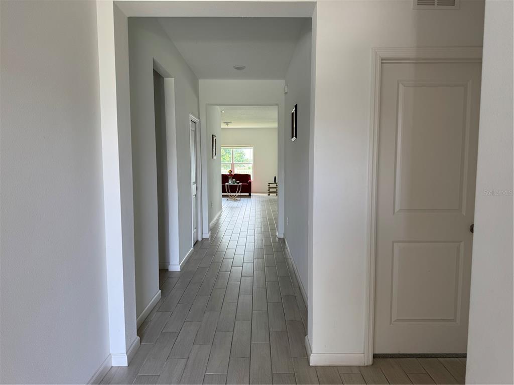 A long hallway with light gray tile flooring leads toward a room with a window — 1177 TUPELO TRAIL, HAINES CITY, FL