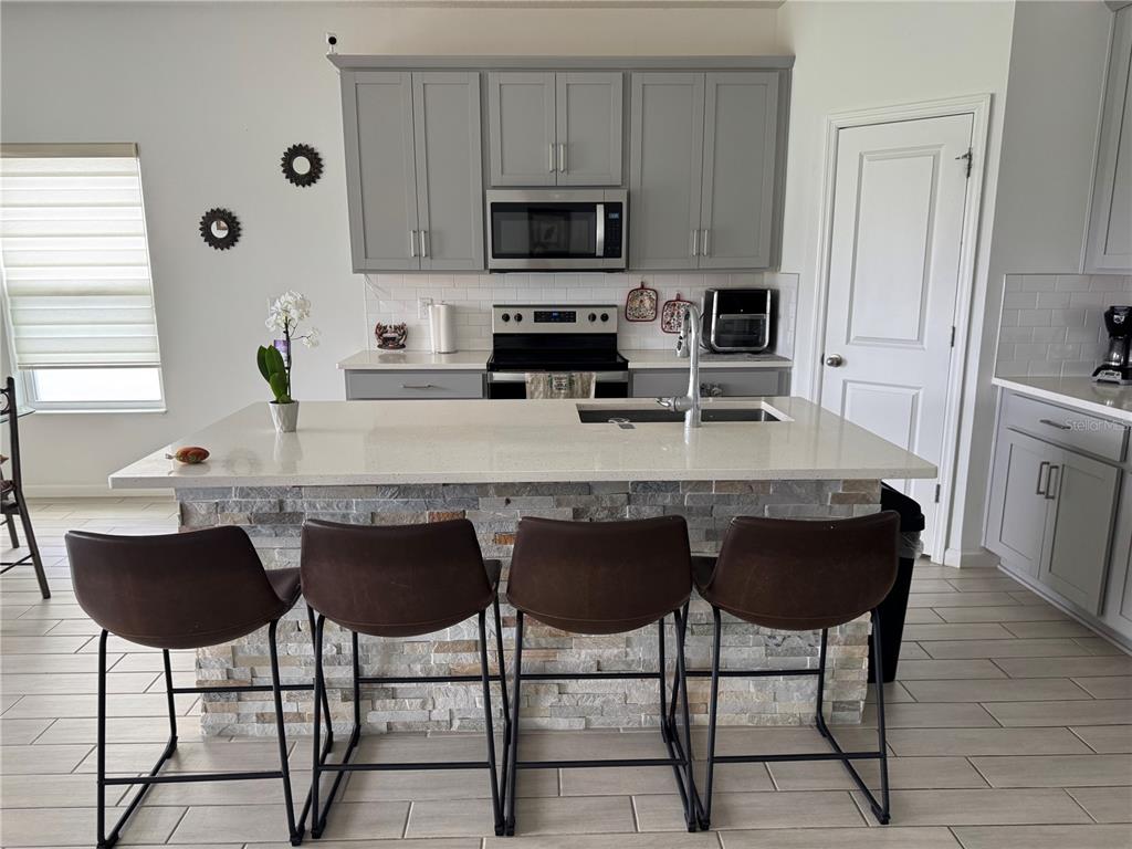A kitchen features a stone-faced island with four barstools, gray cabinetry, and white countertops — 1177 TUPELO TRAIL, HAINES CITY, FL