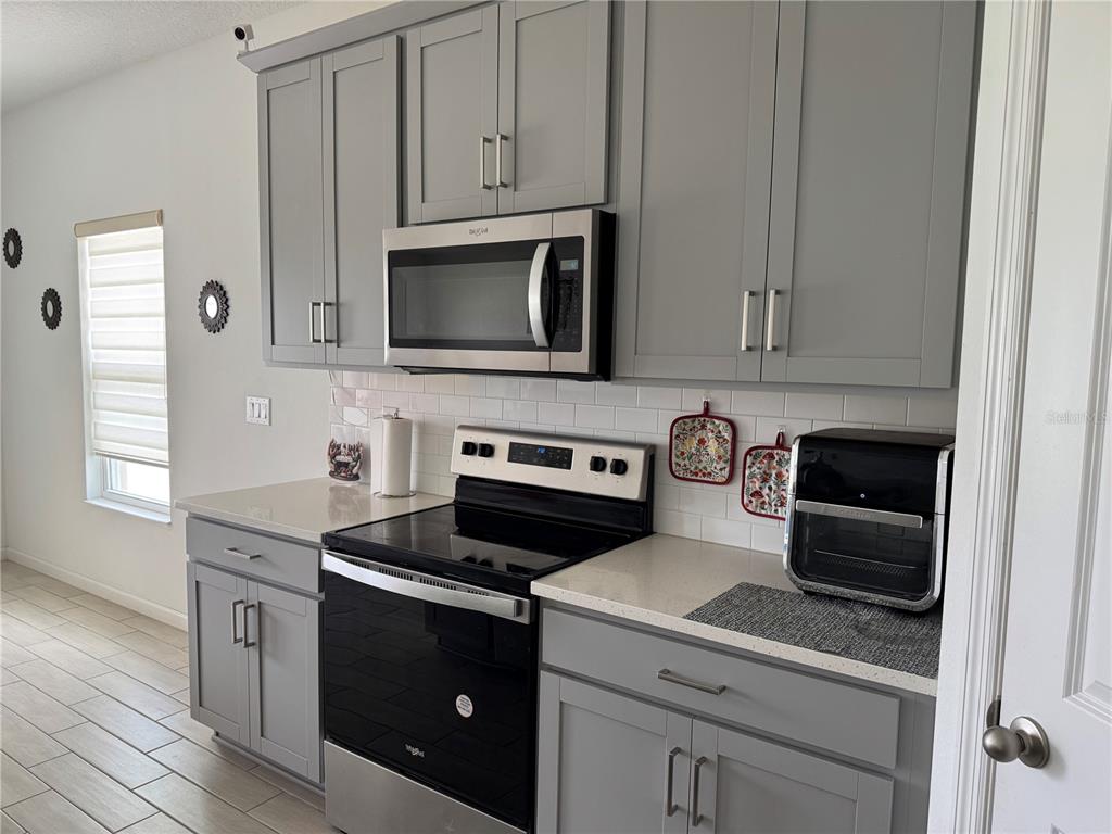 A kitchen features gray cabinets, stainless steel appliances, a white subway tile backsplash, and countertops — 1177 TUPELO TRAIL, HAINES CITY, FL