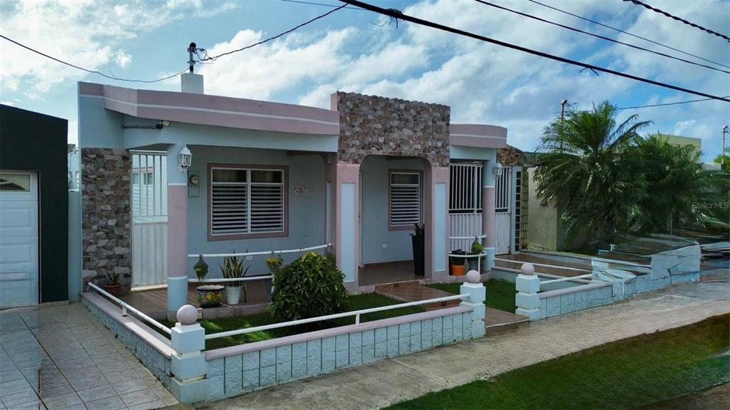 A single-story house with a stone facade, pink trim, and a low concrete perimeter wall — A11 BO ISLOTE, COSTA ATLANTICO, ARECIBO, PR