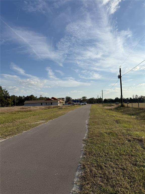 A paved road leads toward a house under construction in a rural, grassy field — 14950 MIM PLACE, DADE CITY, FL