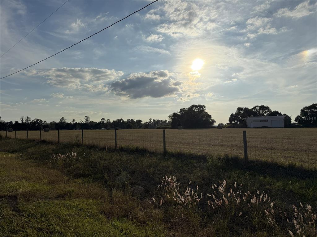 A wire fence borders a large, open field under a bright, cloudy sky — 14950 MIM PLACE, DADE CITY, FL