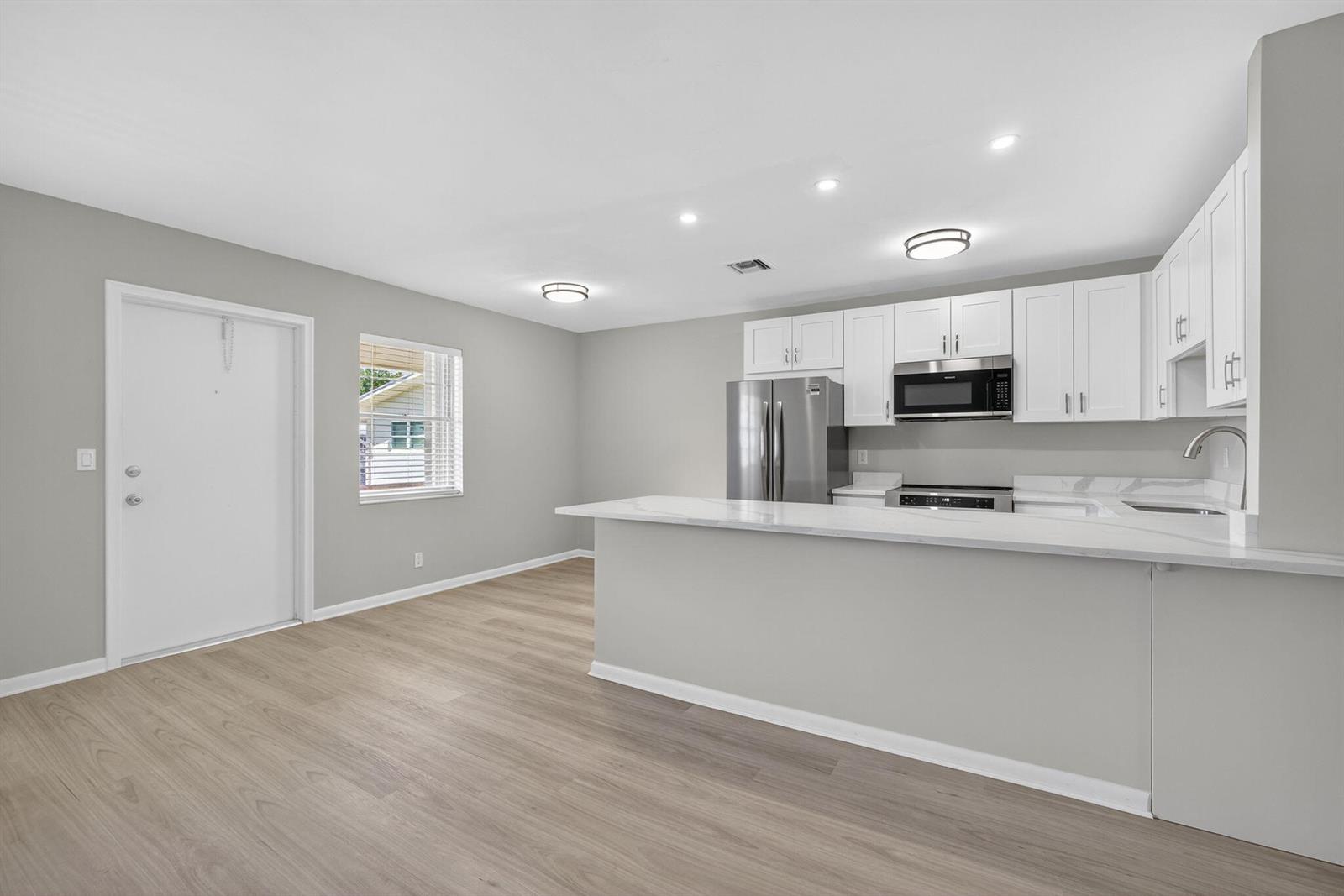 A kitchen with white cabinets, stainless steel appliances, and a peninsula island overlooks a living area — 42 Easthampton B, West Palm Beach FL 33417, WEST PALM BEACH, FL
