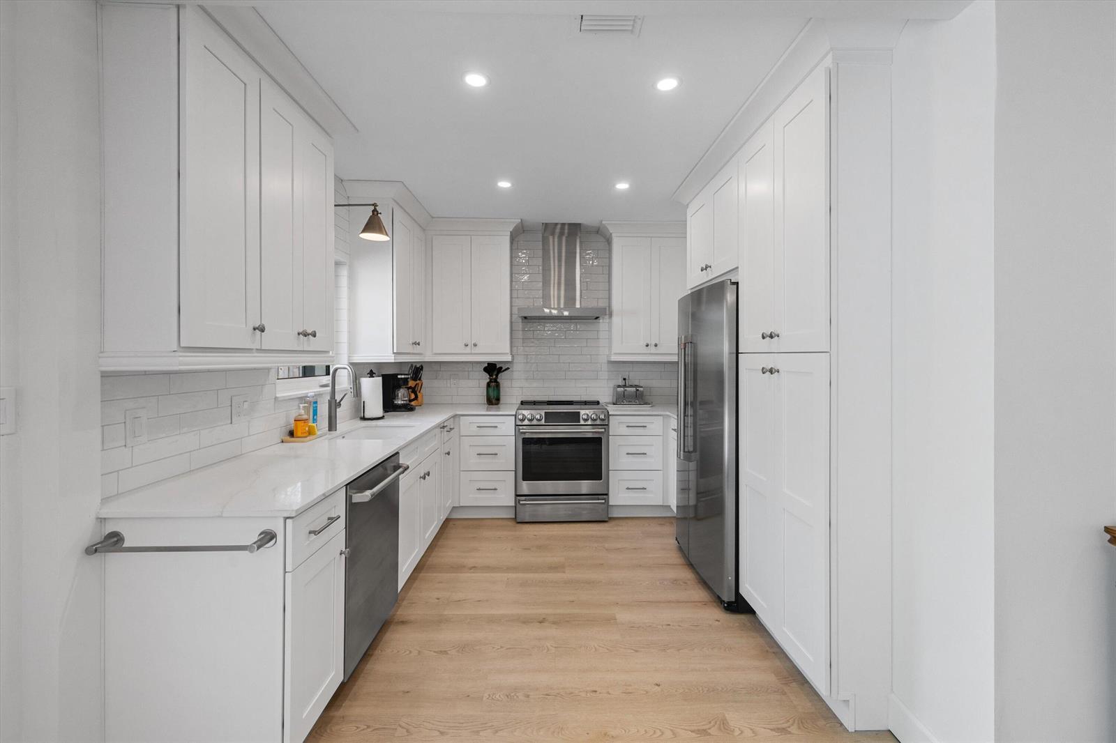 A galley kitchen features white cabinets, stainless steel appliances, subway tile backsplash, and wood flooring — 611 N Palmway, FL 33460, FL