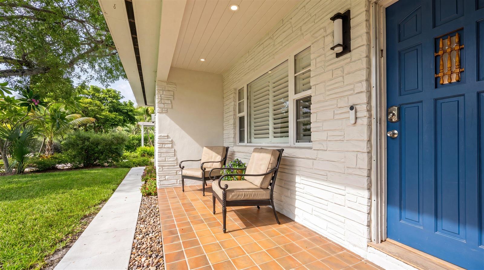 A covered front porch features tiled flooring, two chairs, and a blue front door — 611 N Palmway, FL 33460, FL