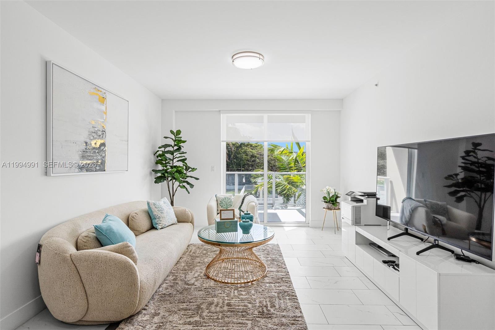 A bright living room features a beige sofa, glass coffee table, and a large television — 1850 Monroe St # 205, Hollywood FL 33020, HOLLYWOOD, FL