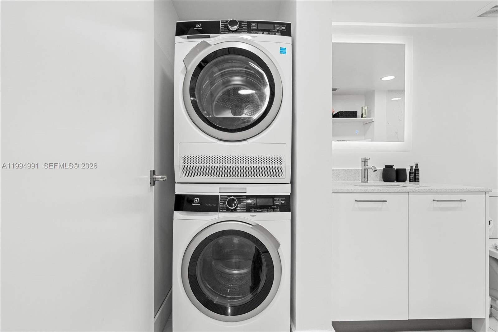 A stacked Electrolux washer and dryer unit sits in a white bathroom next to a vanity — 1850 Monroe St # 205, Hollywood FL 33020, HOLLYWOOD, FL