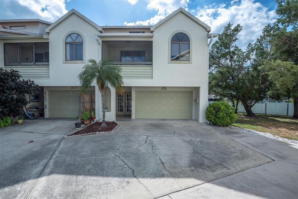 A two-story townhouse exterior features a concrete driveway, two garages, and a screened-in balcony — 534 WALDEN COURT, DUNEDIN, FL