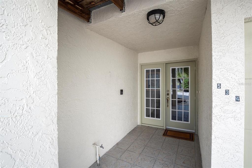 A covered entryway features a light green double door, tiled flooring, and white stucco walls — 534 WALDEN COURT, DUNEDIN, FL