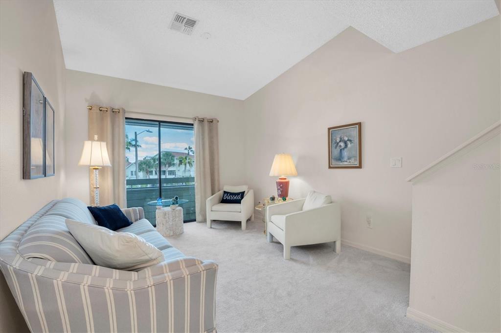 A living room features a striped sofa, two white armchairs, and a sliding glass door — 534 WALDEN COURT, DUNEDIN, FL