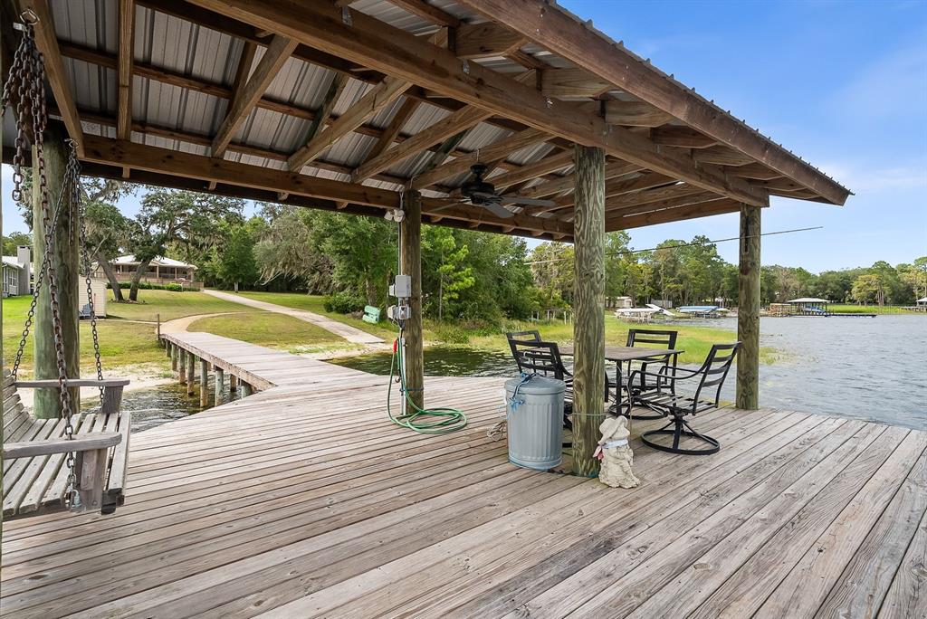 A wooden boat dock features a covered seating area with a swing and patio furniture — 8449 LILLY LAKE ROAD, MELROSE, FL