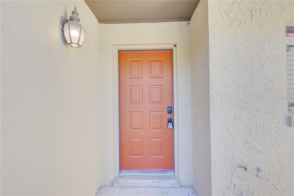 An orange front door with eight panels is set into a beige stucco exterior wall — 506 CLUB DRIVE, WINTER SPRINGS, FL