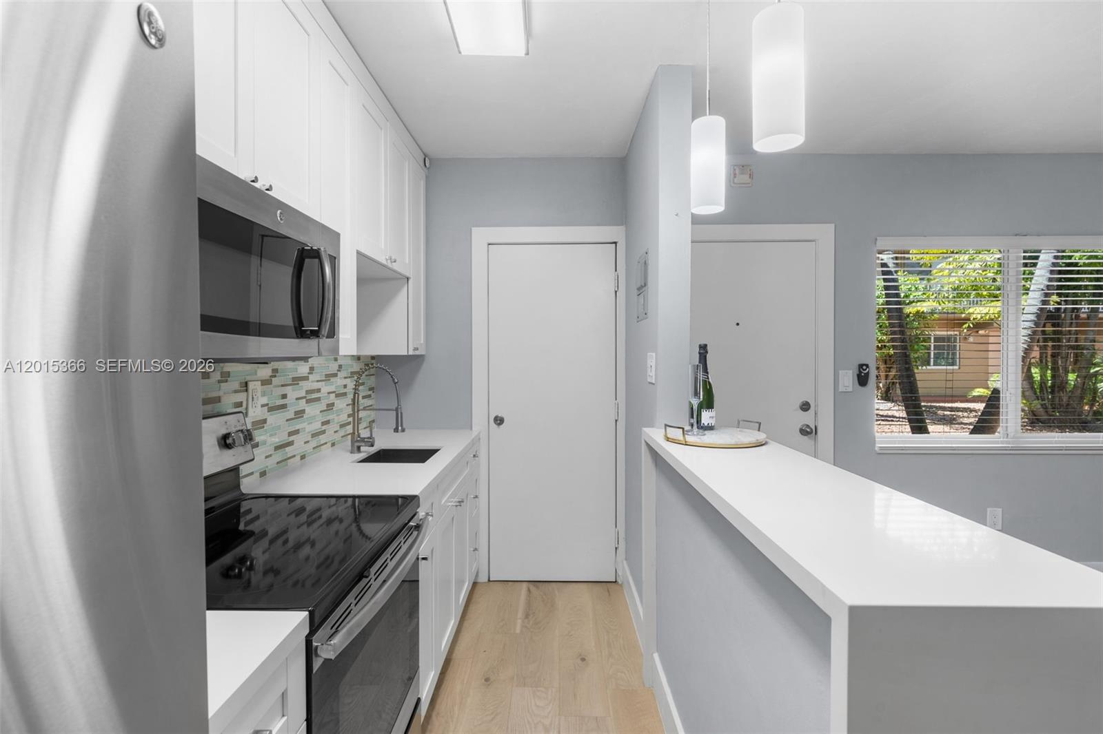 A modern kitchen features white cabinetry, a tiled backsplash, stainless steel appliances, and a breakfast bar — 6330 SW 79th St # 4, South Miami FL 33143, SOUTH MIAMI, FL