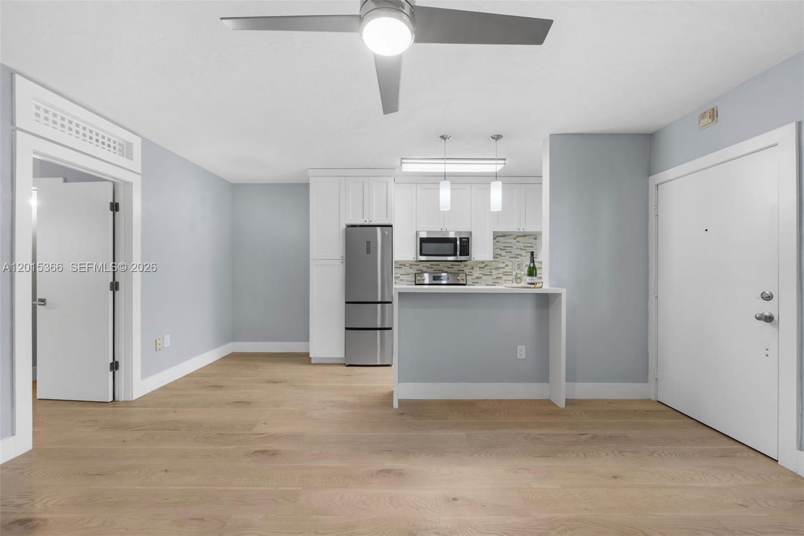 This kitchen and living area features light blue walls, white cabinetry, and light wood flooring — 6330 SW 79th St # 4, South Miami FL 33143, SOUTH MIAMI, FL
