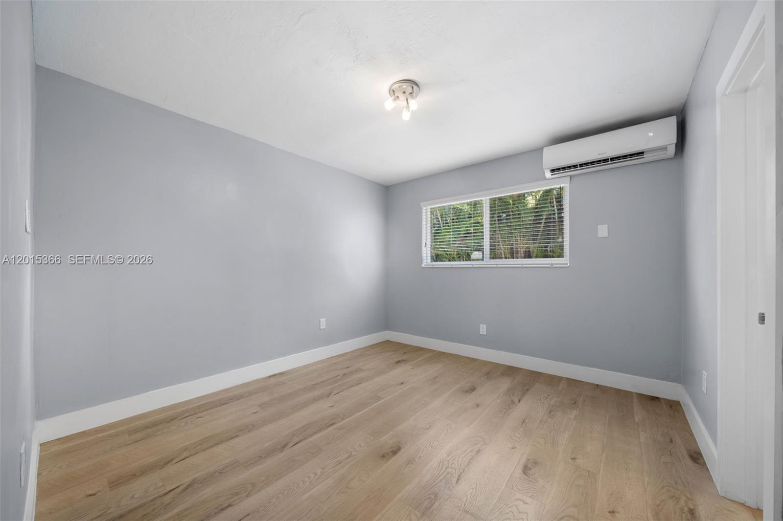 An empty bedroom features light gray walls, wood-look flooring, a window, and a wall-mounted air conditioner — 6330 SW 79th St # 4, South Miami FL 33143, SOUTH MIAMI, FL