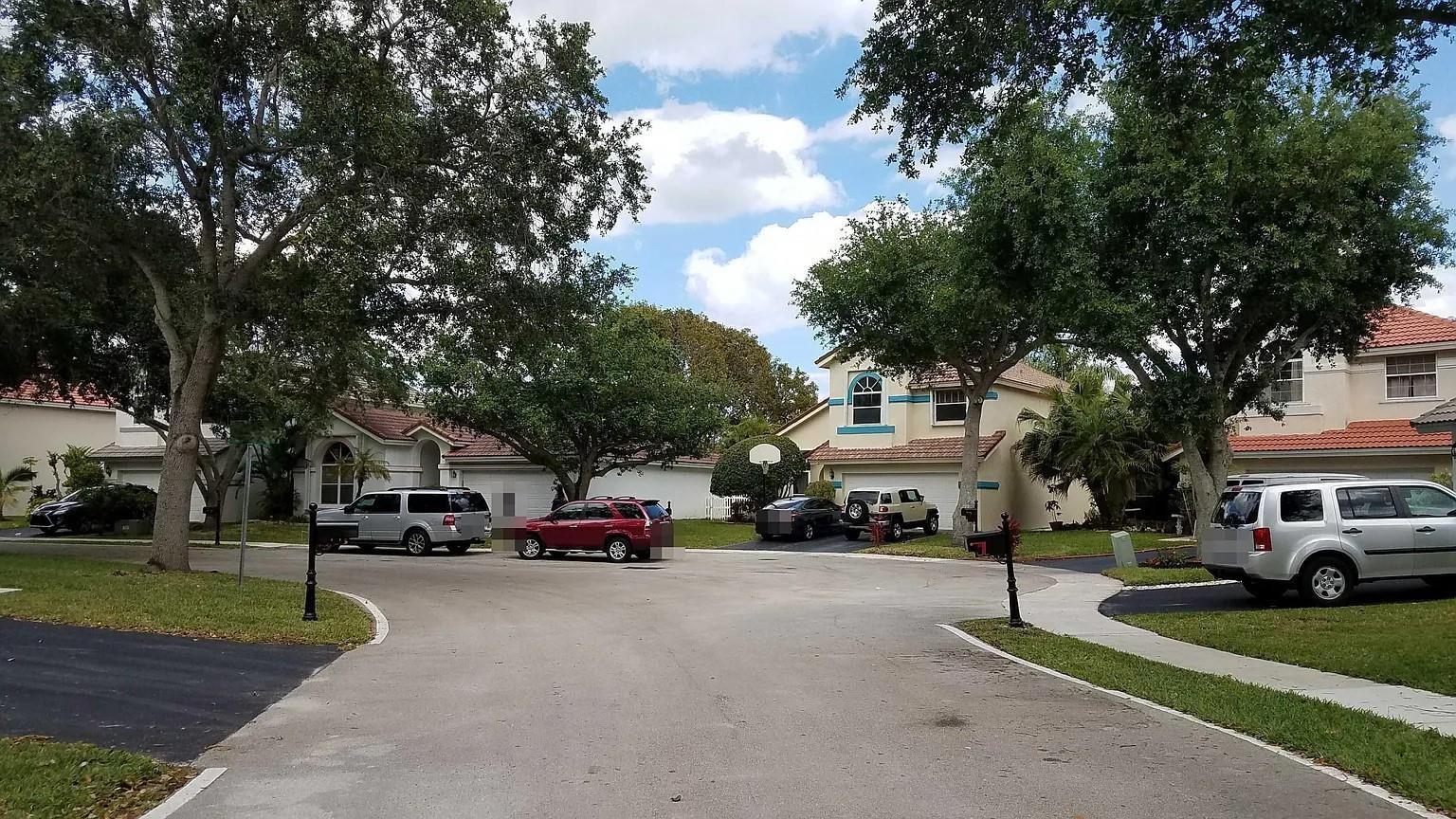 A residential street view showing several houses, parked cars, and mature trees under a blue sky — 6930 NW 28th Street, Margate FL 33063, MARGATE, FL
