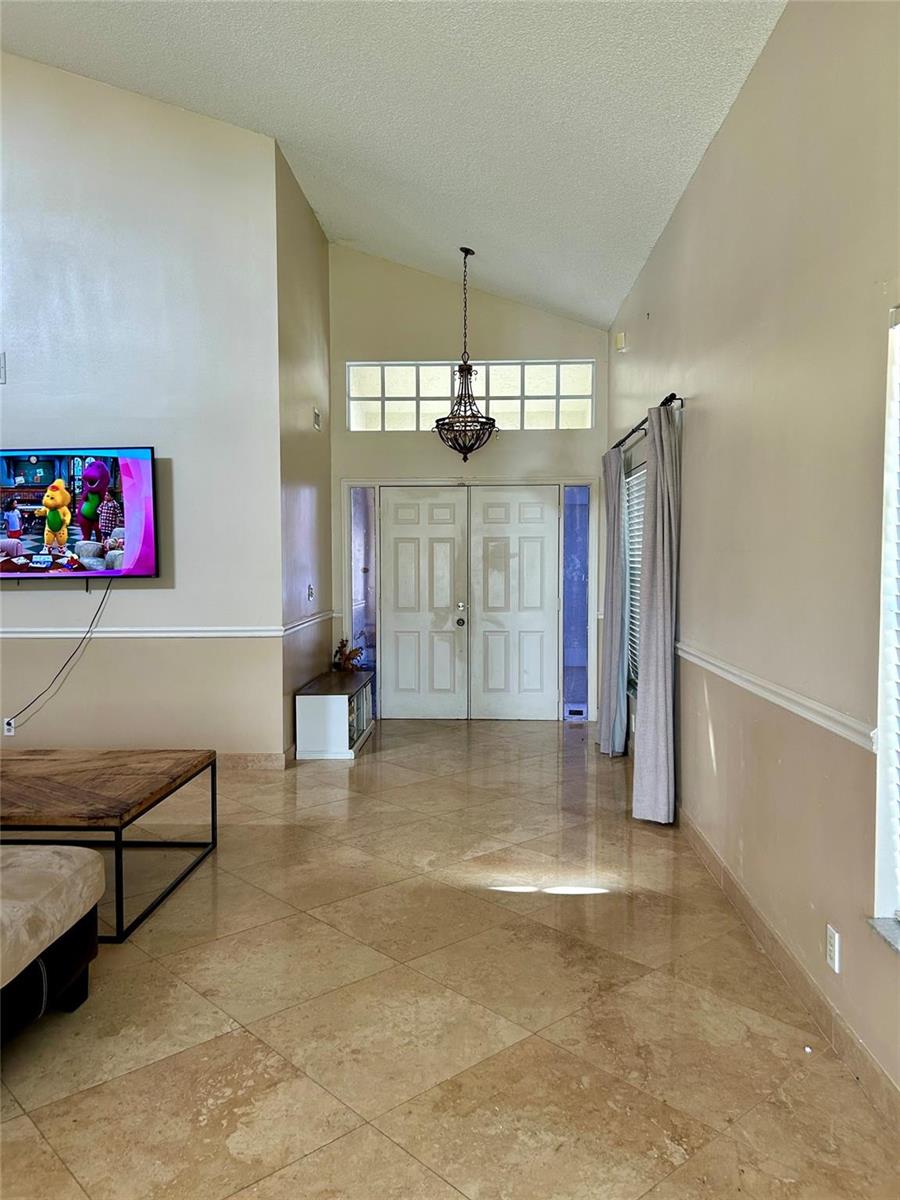 A living room with tile flooring, a vaulted ceiling, and double front entry doors — 6930 NW 28th Street, Margate FL 33063, MARGATE, FL