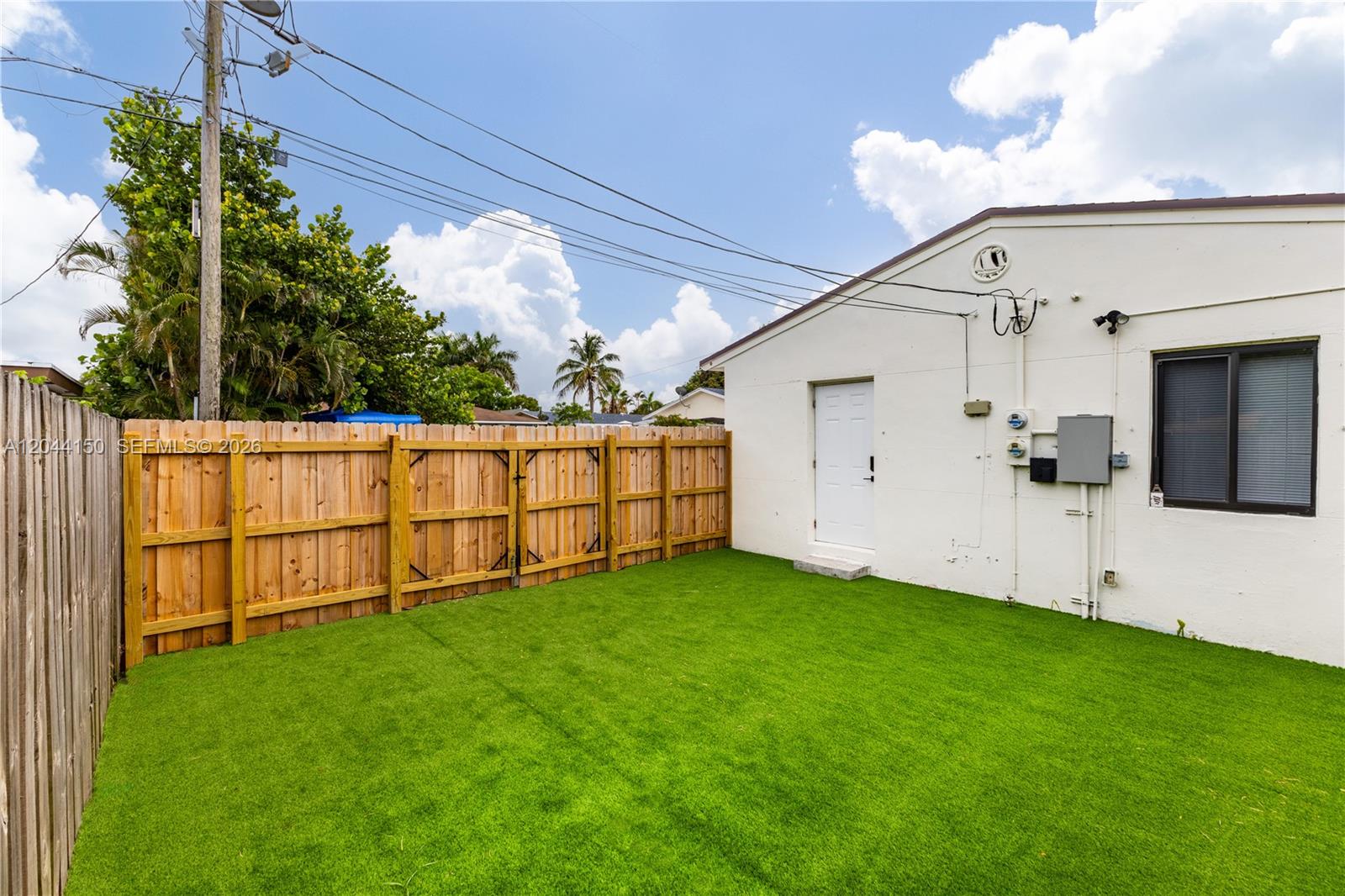 A backyard features artificial turf, a wooden fence, and the exterior wall of a house — 1918 Taft St, Hollywood FL 33020, HOLLYWOOD, FL