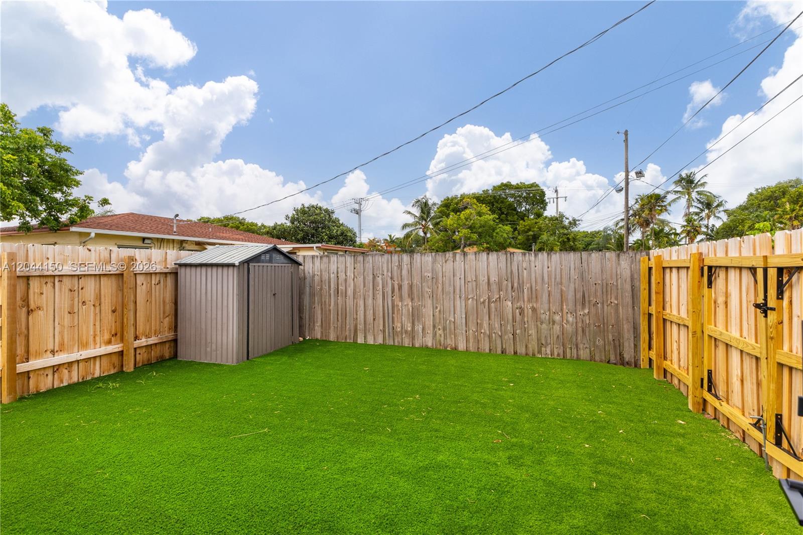 A fenced backyard features artificial turf, a small metal storage shed, and surrounding trees — 1918 Taft St, Hollywood FL 33020, HOLLYWOOD, FL
