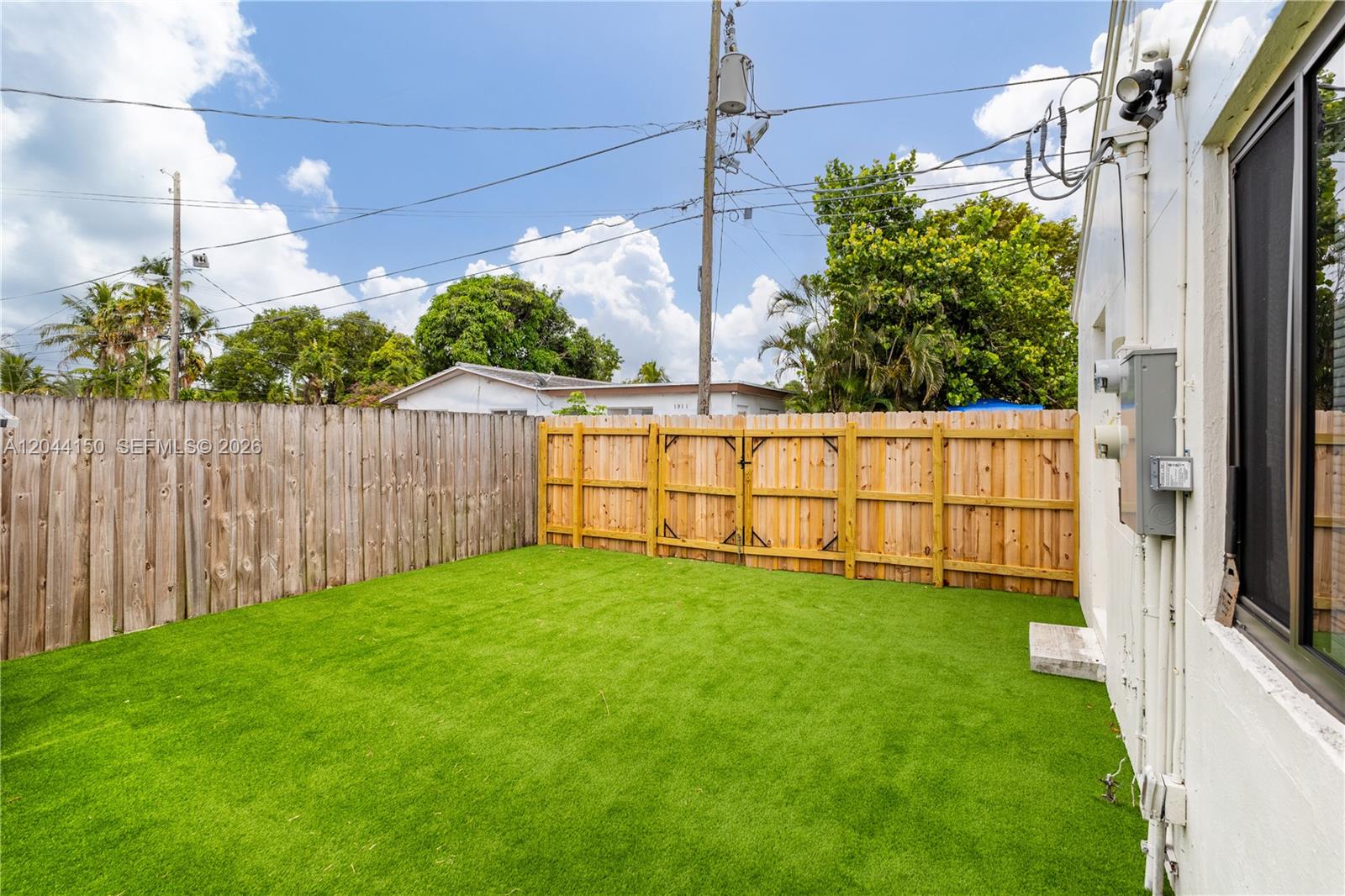 A fenced backyard features artificial turf and a white exterior wall with a window — 1918 Taft St, Hollywood FL 33020, HOLLYWOOD, FL