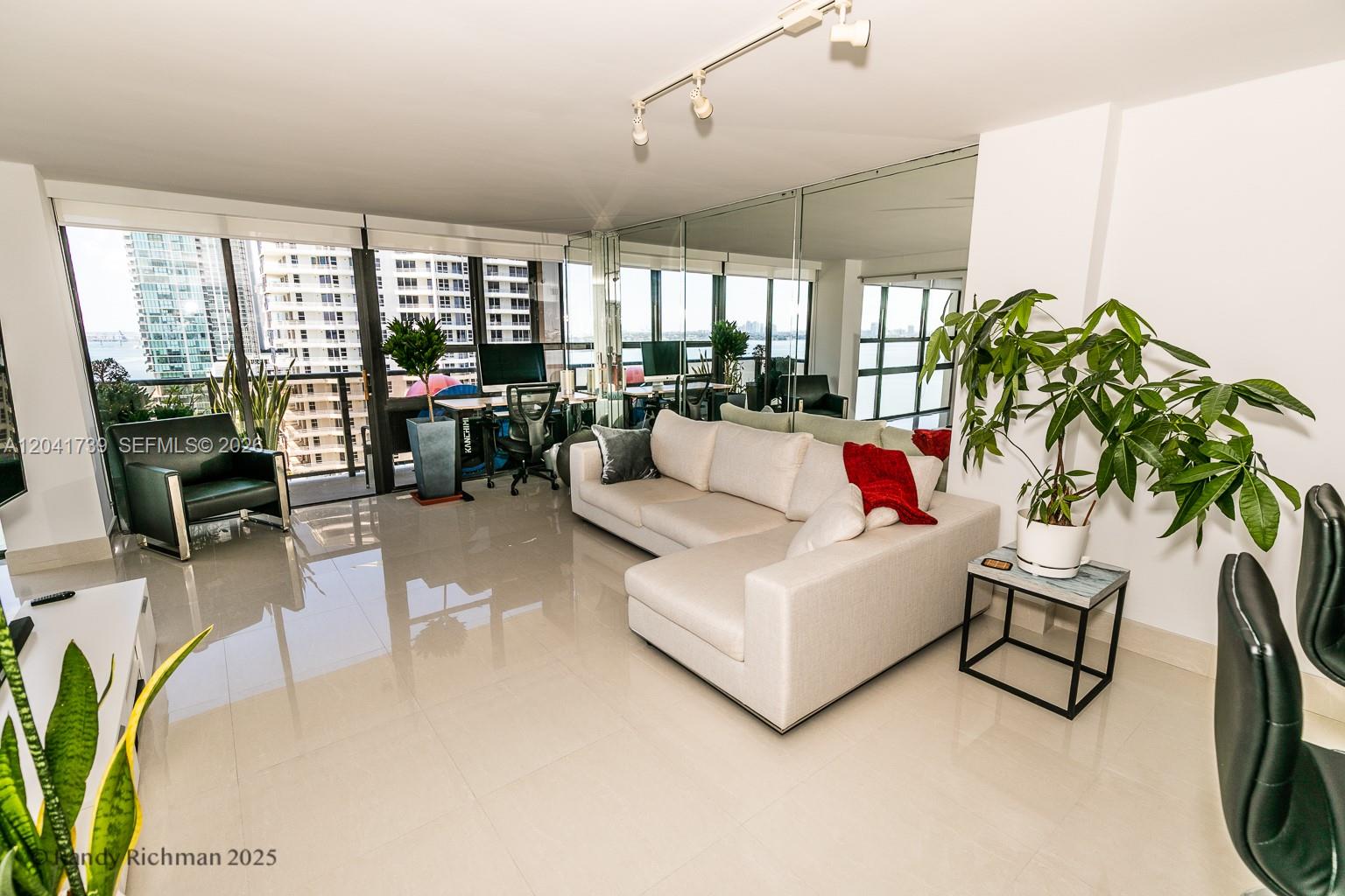 A modern living room features a white sectional sofa, tile flooring, and floor-to-ceiling windows — 600 NE 36th St # 1820, Miami FL 33137, MIAMI, FL