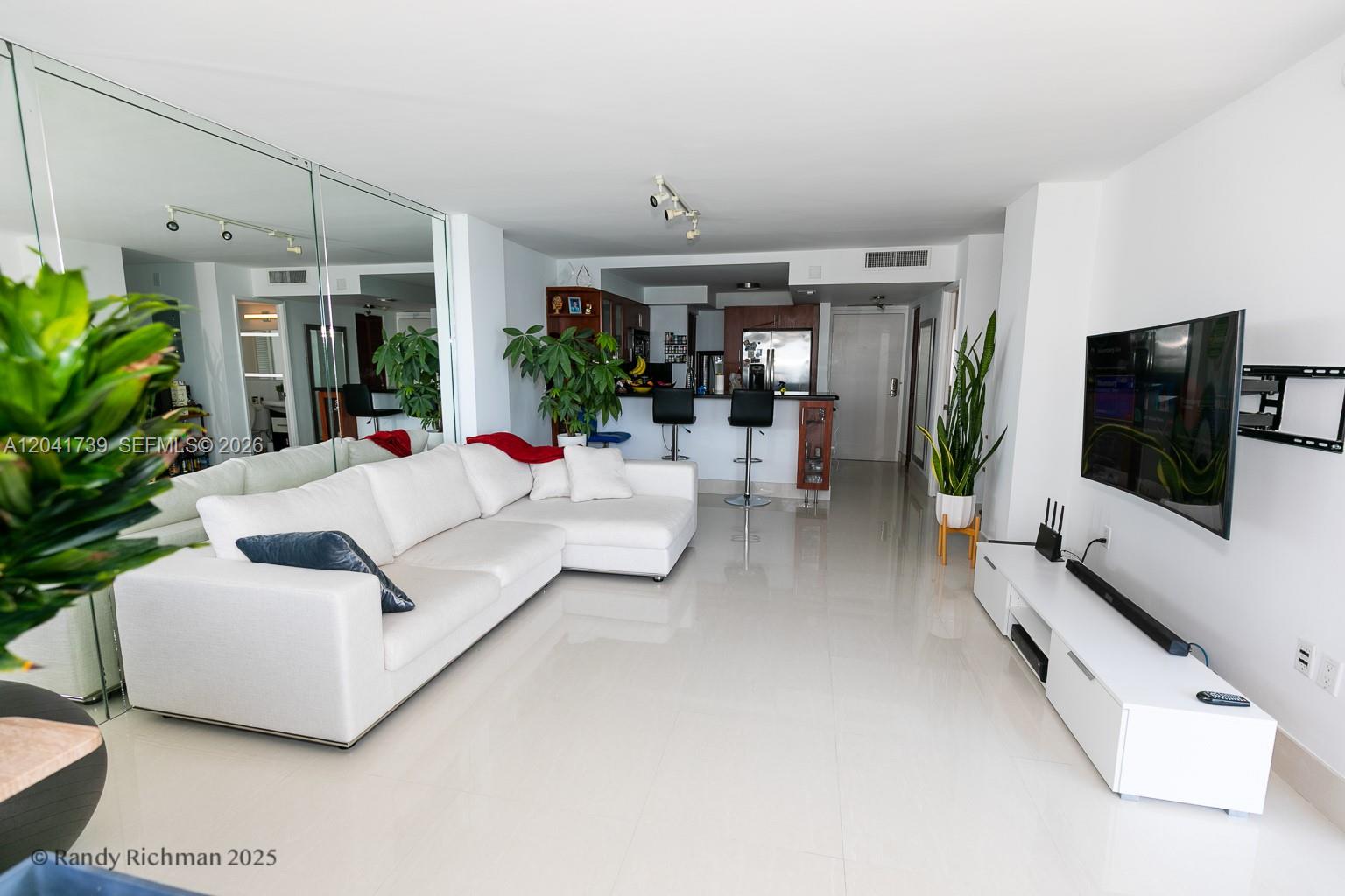 A modern living room features a white sectional sofa, tiled floors, and an open kitchen — 600 NE 36th St # 1820, Miami FL 33137, MIAMI, FL