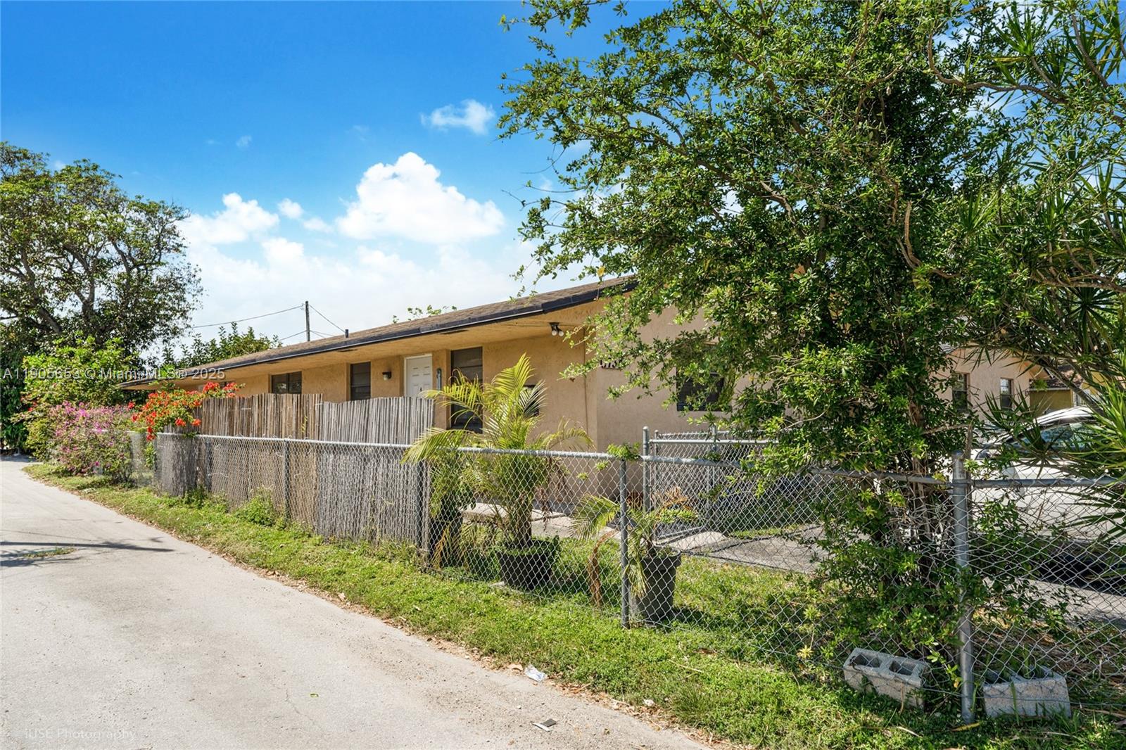 A single-story tan house sits behind a chain-link fence along a paved road — 1734 N 16th Ct, Hollywood FL 33020, HOLLYWOOD, FL
