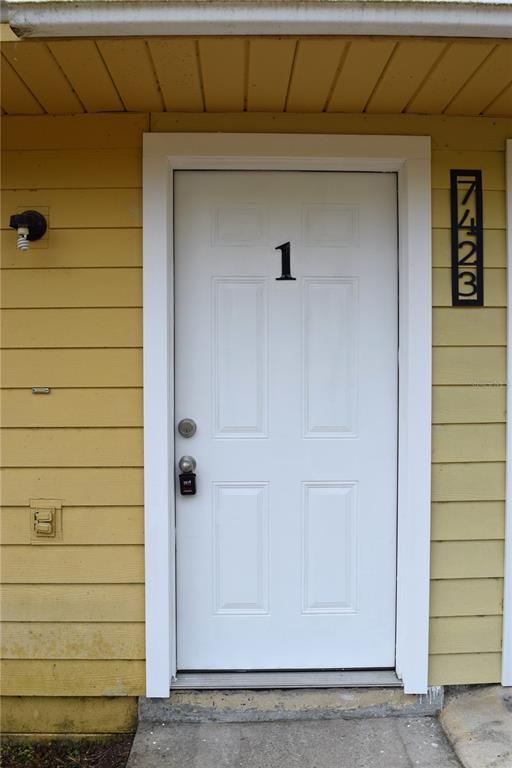 A white front door with the number one is set in yellow horizontal siding — 7423 SW 42ND PLACE, GAINESVILLE, FL