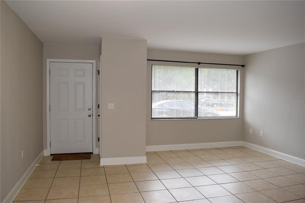 An empty room features beige tile flooring, light gray walls, a white door, and windows — 7423 SW 42ND PLACE, GAINESVILLE, FL