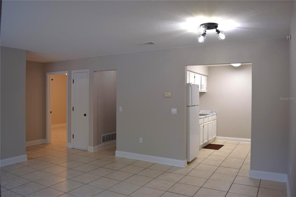 A room with light-colored tile flooring leads to a kitchen area with white cabinets — 7423 SW 42ND PLACE, GAINESVILLE, FL