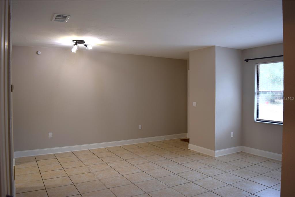 An empty room features beige walls, light-colored floor tiles, a ceiling light fixture, and a window — 7423 SW 42ND PLACE, GAINESVILLE, FL