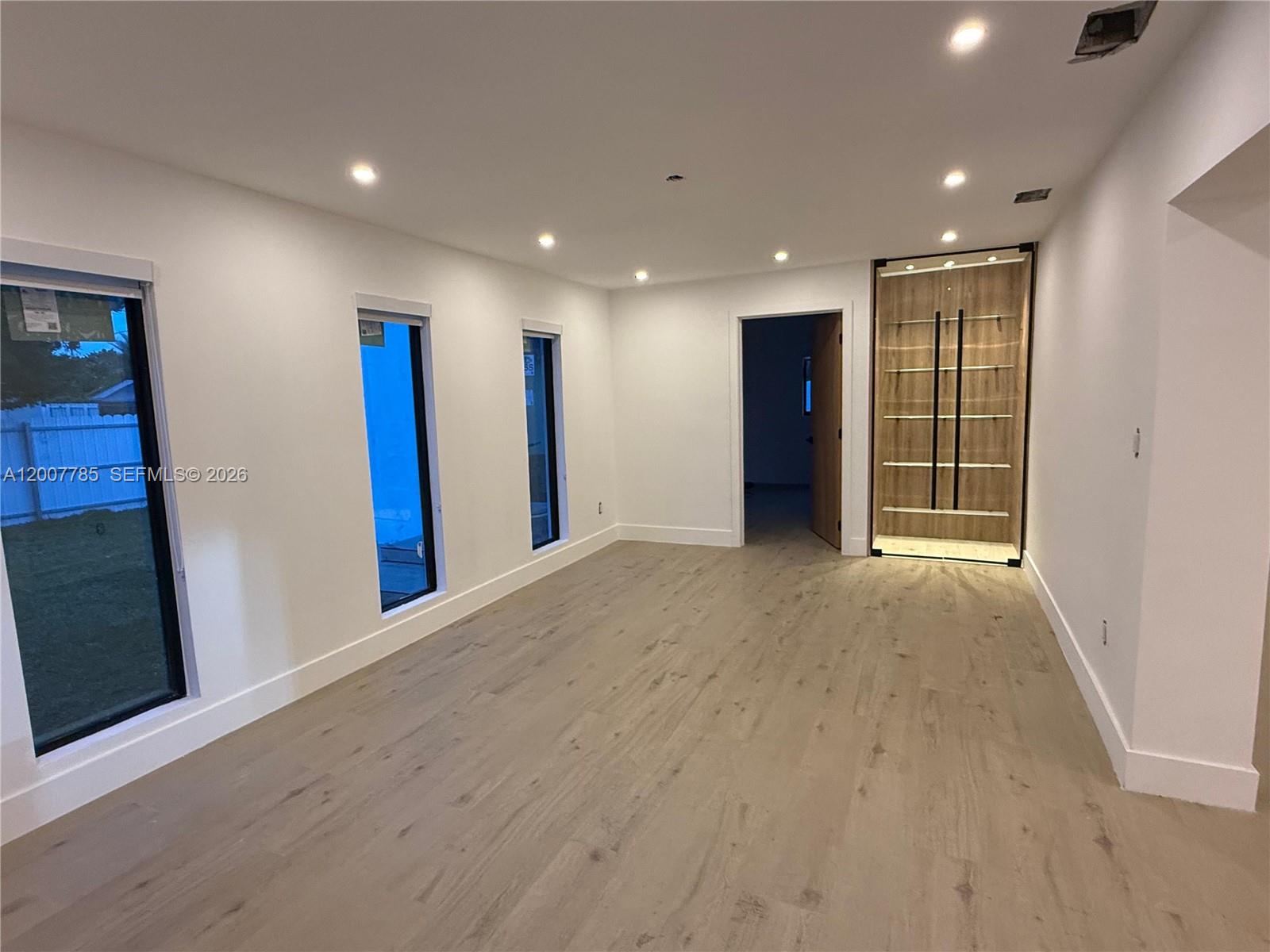A room with light wood flooring, white walls, three tall windows, and a built-in display shelf — 12810 SW 18th St, Miami FL 33175, MIAMI, FL