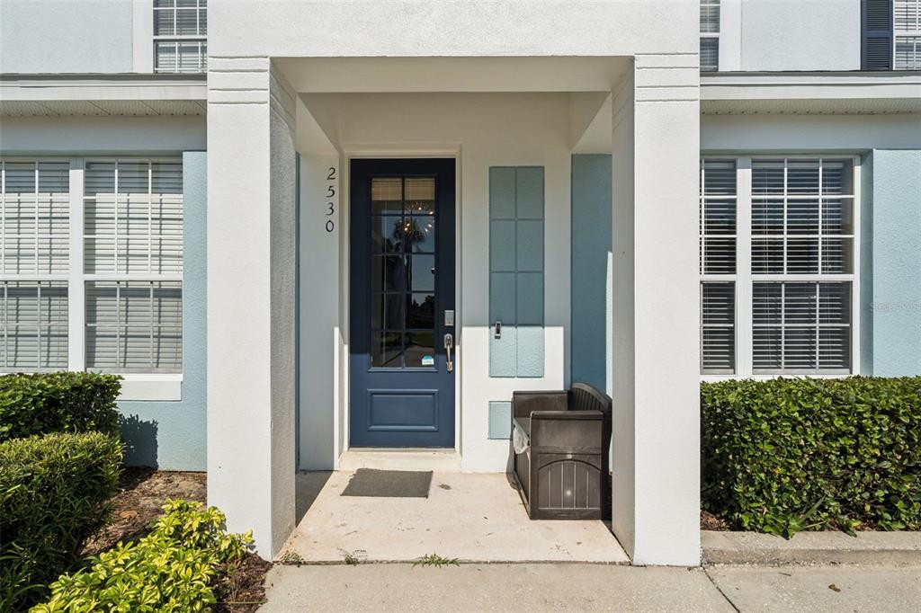 The exterior entrance features a dark blue front door, a concrete porch, and a storage bench — 2530 MANESHAW LANE, KISSIMMEE, FL