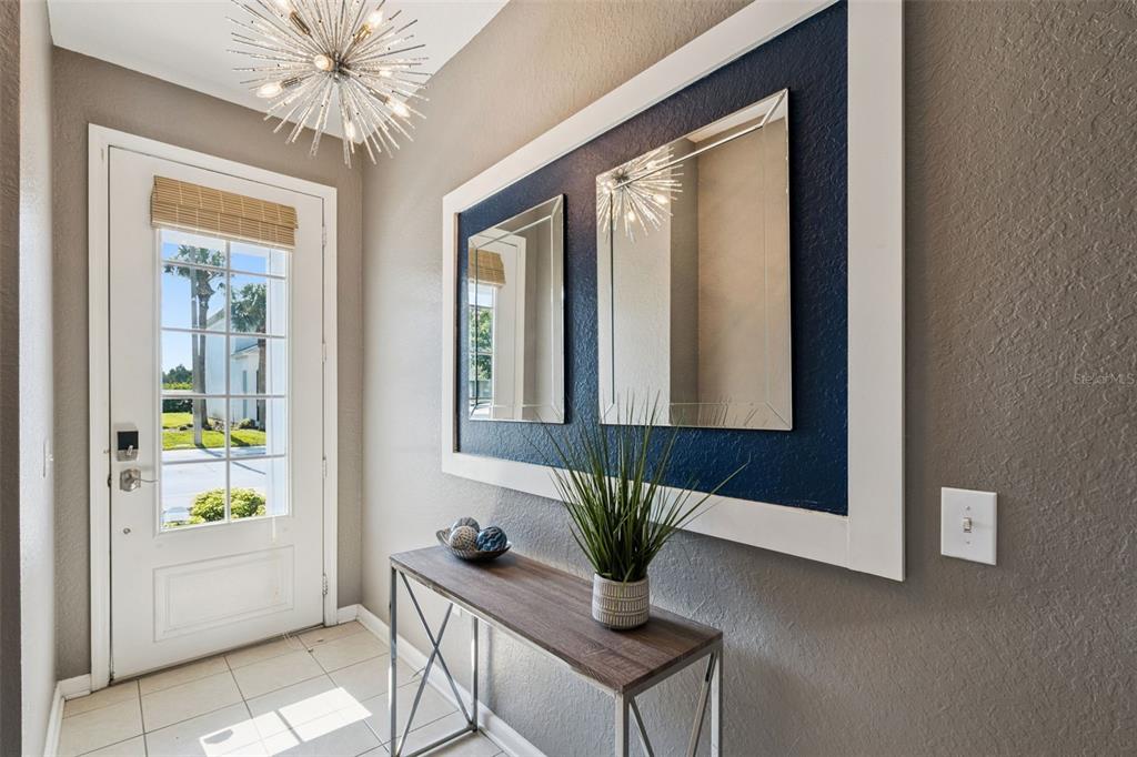 An entryway features a console table, two mirrors on a blue accent wall, and a chandelier — 2530 MANESHAW LANE, KISSIMMEE, FL