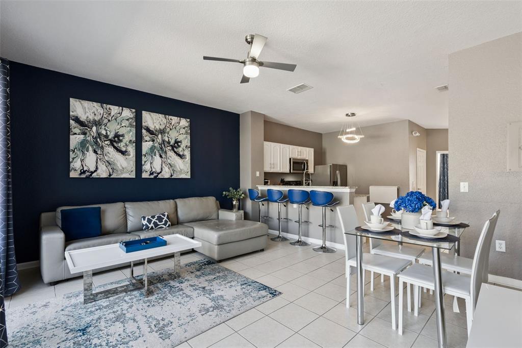 A living room and dining area feature a navy accent wall, gray sofa, and tile flooring — 2530 MANESHAW LANE, KISSIMMEE, FL