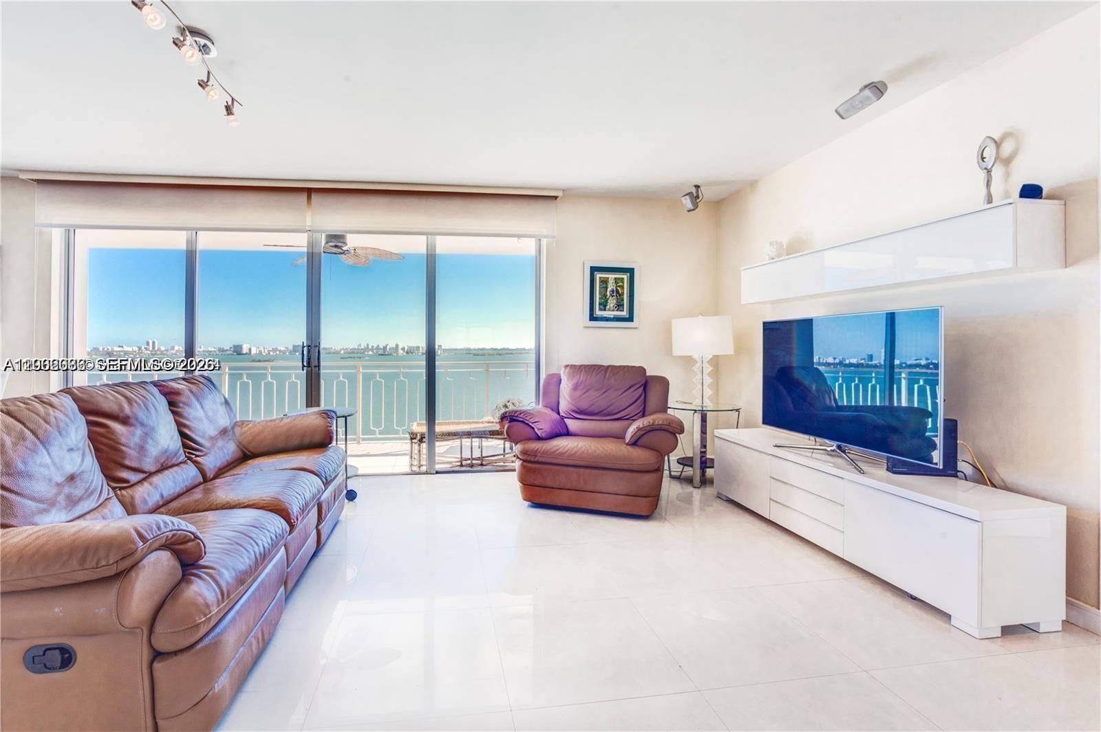 A living room features brown leather furniture, white tile floors, and a balcony with water views — 11111 Biscayne Blvd # 18E, Miami FL 33181, MIAMI, FL