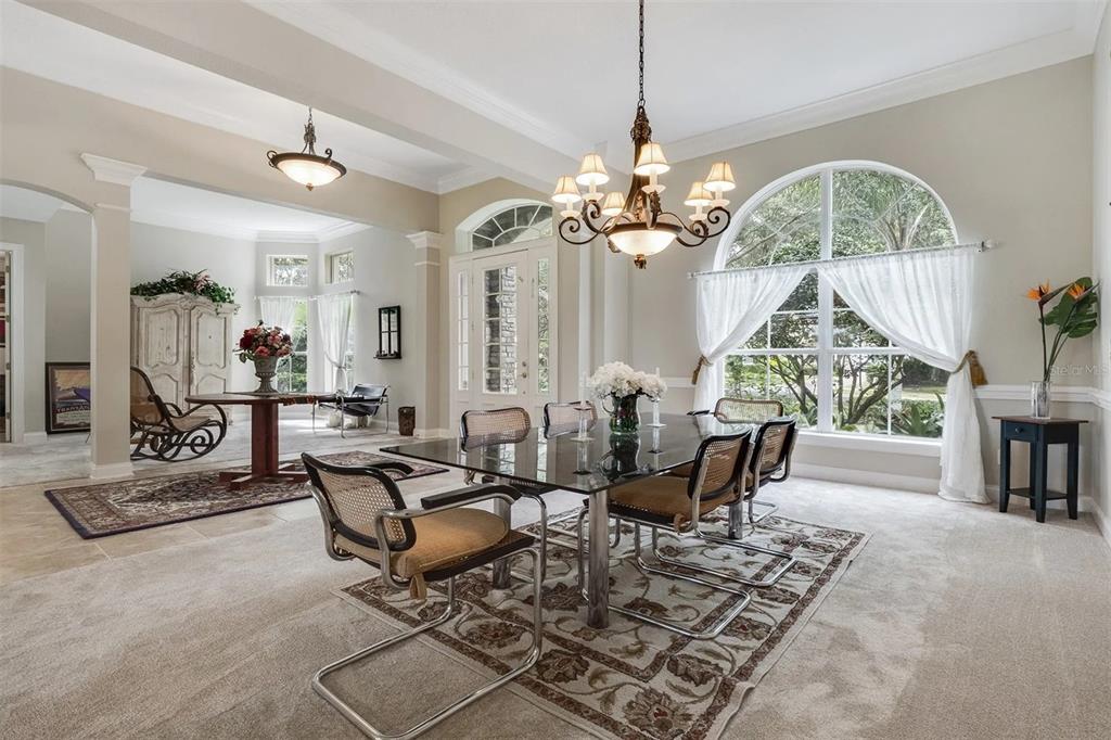 A dining room with a glass table, chandelier, and large arched window overlooking greenery — 25551 HAWKS RUN LANE, SORRENTO, FL
