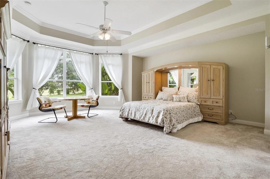 A spacious bedroom features a large bed with a built-in headboard, carpeted floors, and windows — 25551 HAWKS RUN LANE, SORRENTO, FL